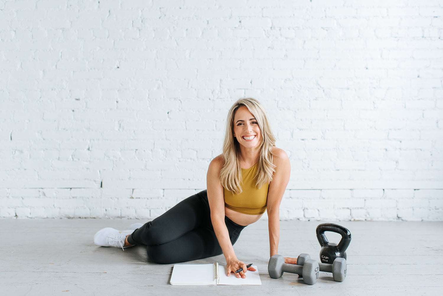 Woman planning her exercise  with dumbbells and a kettlebell in a home gym setting.